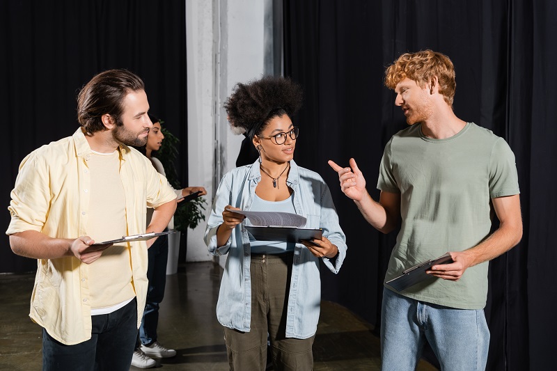 Three people with clip boards talking back stage