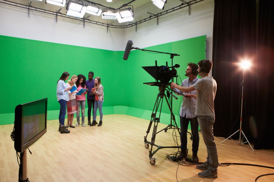 Photo shows group of teenagers huddled together reading scripts in front of a greenscreen