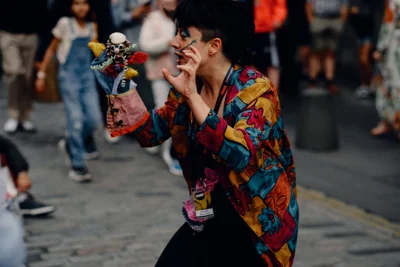 photo shows close up of female puppeteer in bright shirt performing on Edinburgh's royal mile with patchwork puppet