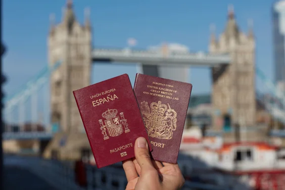 photo shows hand holding a Spanish and a British passport in front of tower bridge 