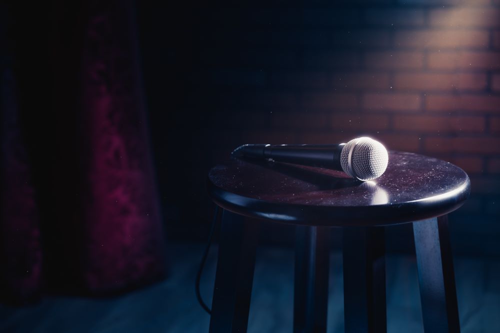 Photo shows stool on stage with a microphone perched on top of the seat