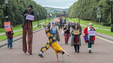 A stilt walker, circus performer, pantomime elf and other performers walking to Stormont