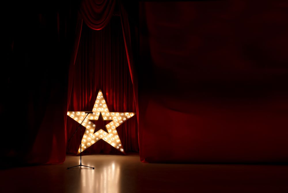 Photo shows stage empty stage with red velvet curtains, a large lit up star and microphone  stand