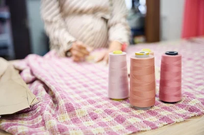 Pregnant woman sat at a table with a gingham cloth and pink coloured cotton threads. 