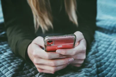 Woman with long blonde hair looking at a red iPhone. 